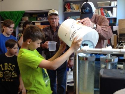 students assist hatchery members to fill the hatchery container with fertilizes eggs at the school hatchery